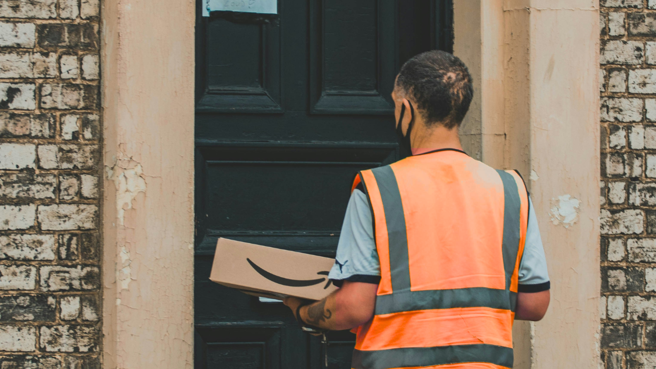 Delivery worker in an orange vest holding an Amazon package, representing precise and effective Amazon management services.
