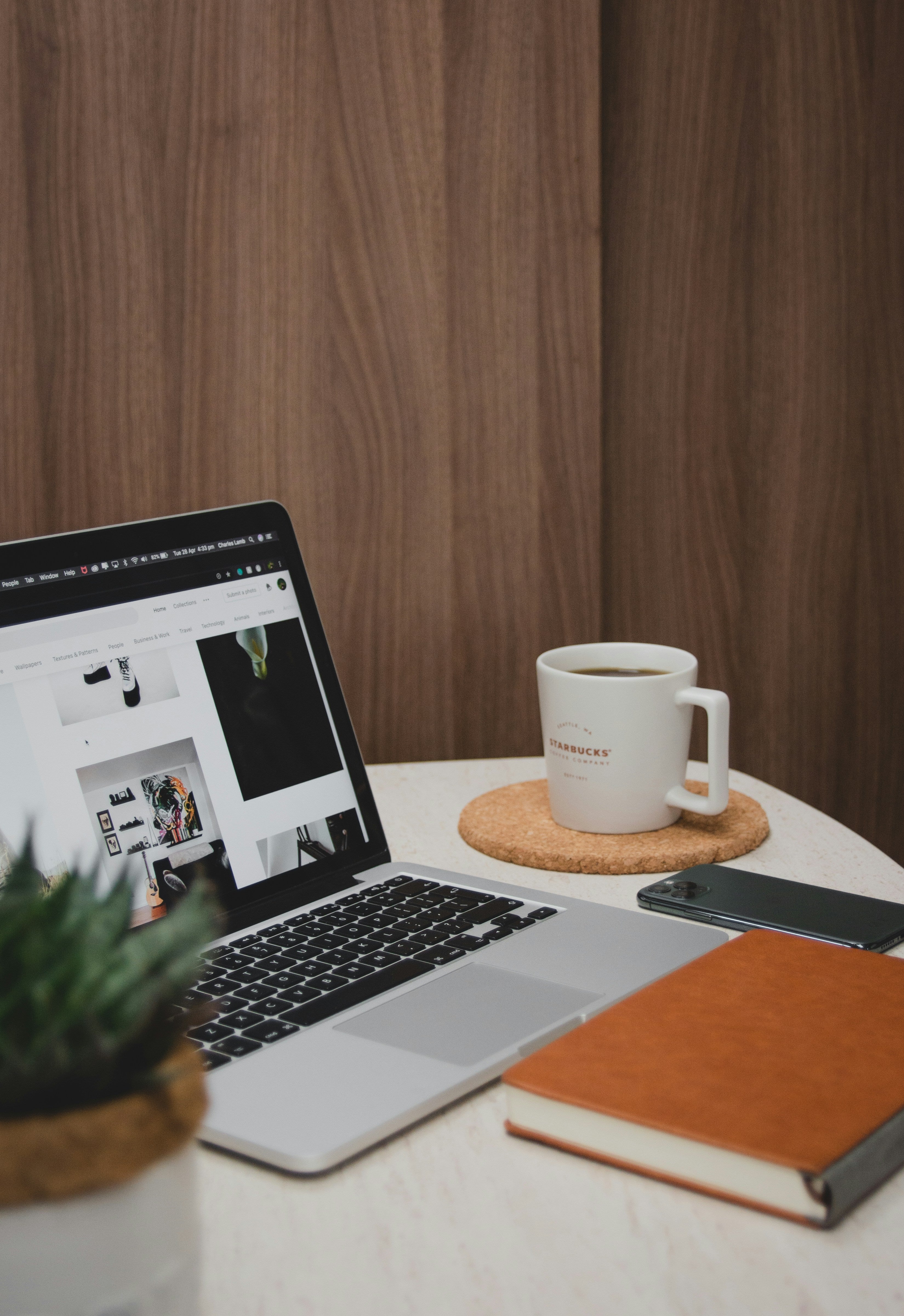 A sleek workspace featuring a laptop displaying a design page, a Starbucks coffee mug, and a notebook, symbolizing productivity and creativity.